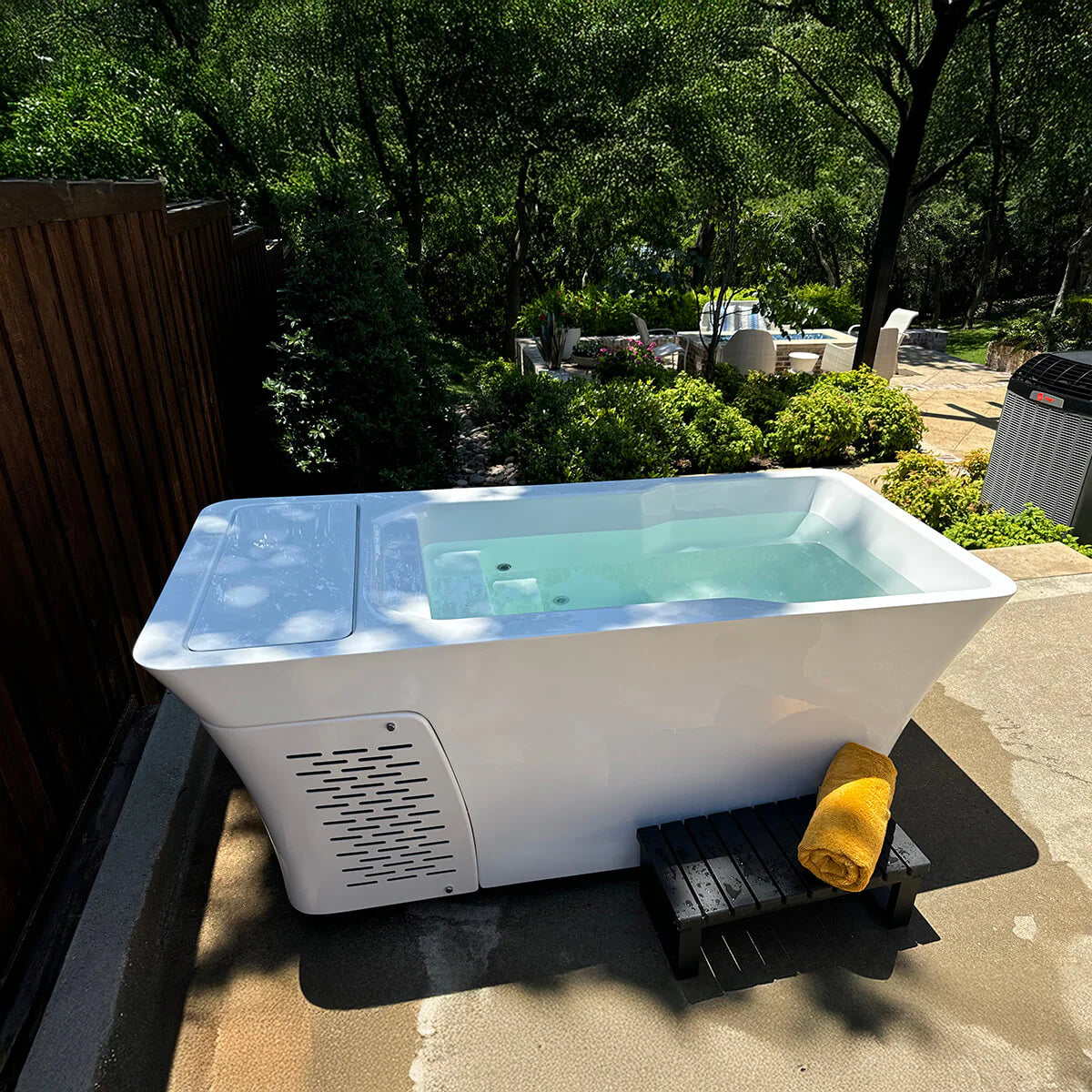 Outdoor plunge with a yellow towel on a wooden platform, surrounded by greenery.