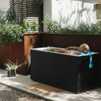 Person lying in a modern outdoor plunge with plants and a wooden deck in the background.
